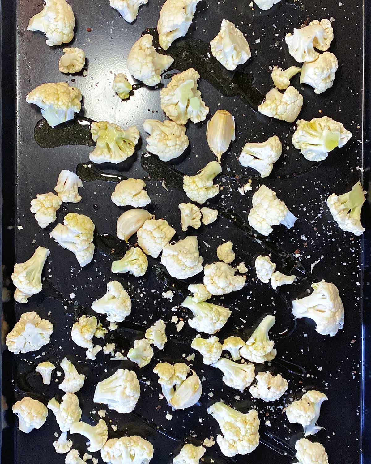 Cauliflower florets and garlic cloves on a large baking tray.