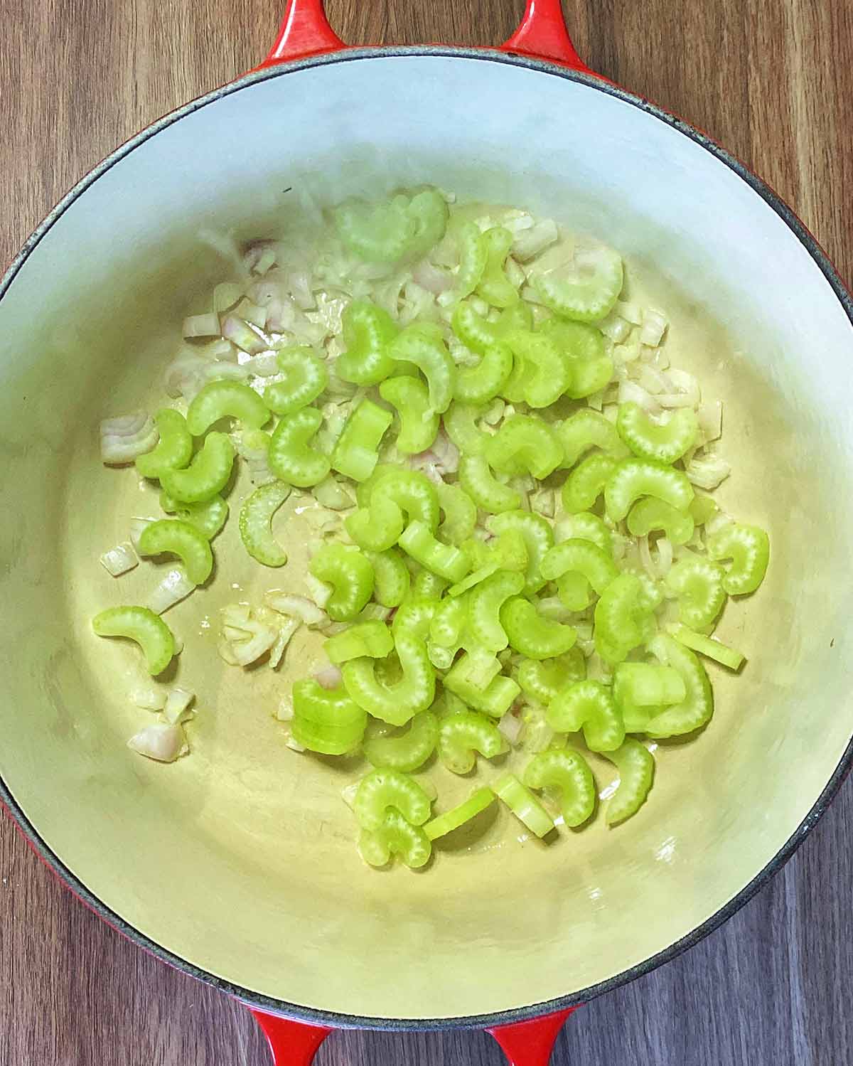 Sliced celery and diced shallots cooking in a large pan.