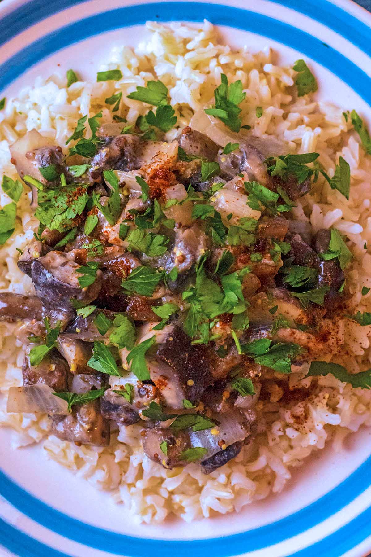 A plate of Stroganoff on top of rice with chopped parsley sprinkled on top.