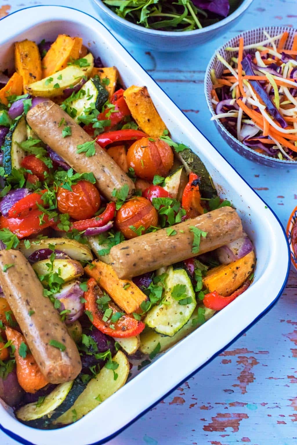 Sausage and vegetable traybake in a white dish.