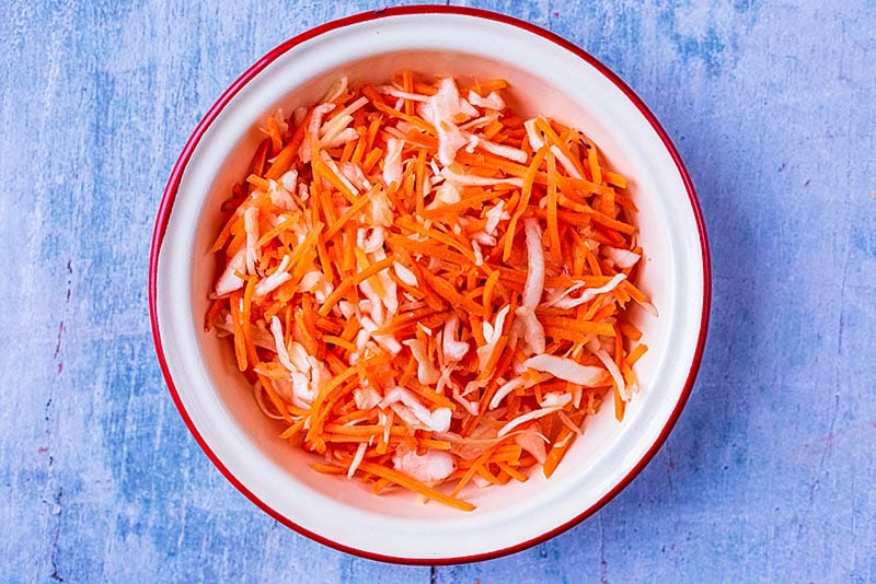 A round bowl containing shredded carrot and shredded white cabbage.