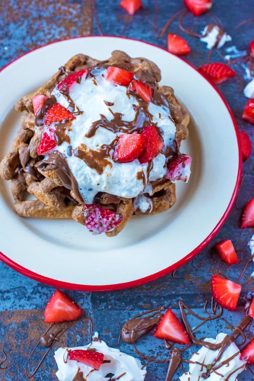 Waffles, cream and strawberries on a plate surrounded by more strawberries and chocolate sauce.