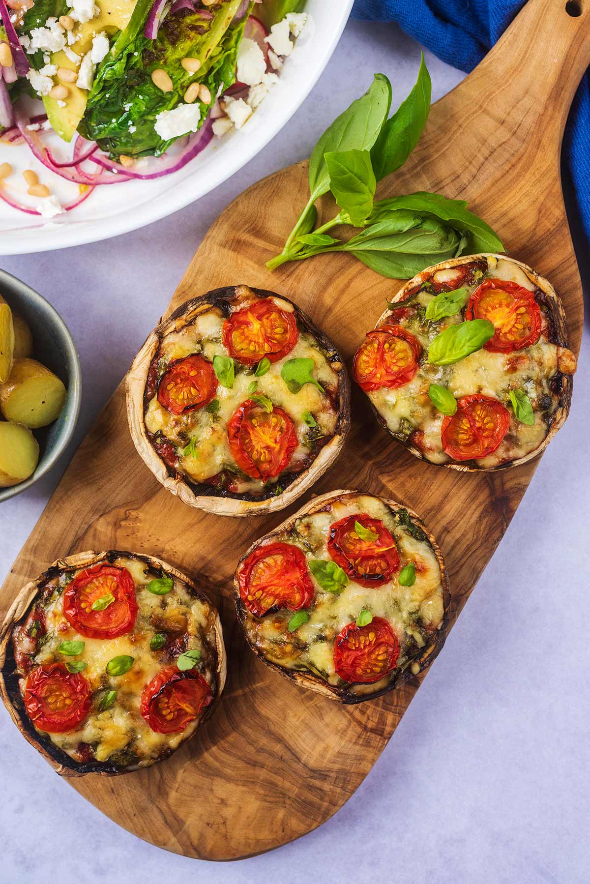 A wooden serving board with four portobello mushroom pizzas on it.