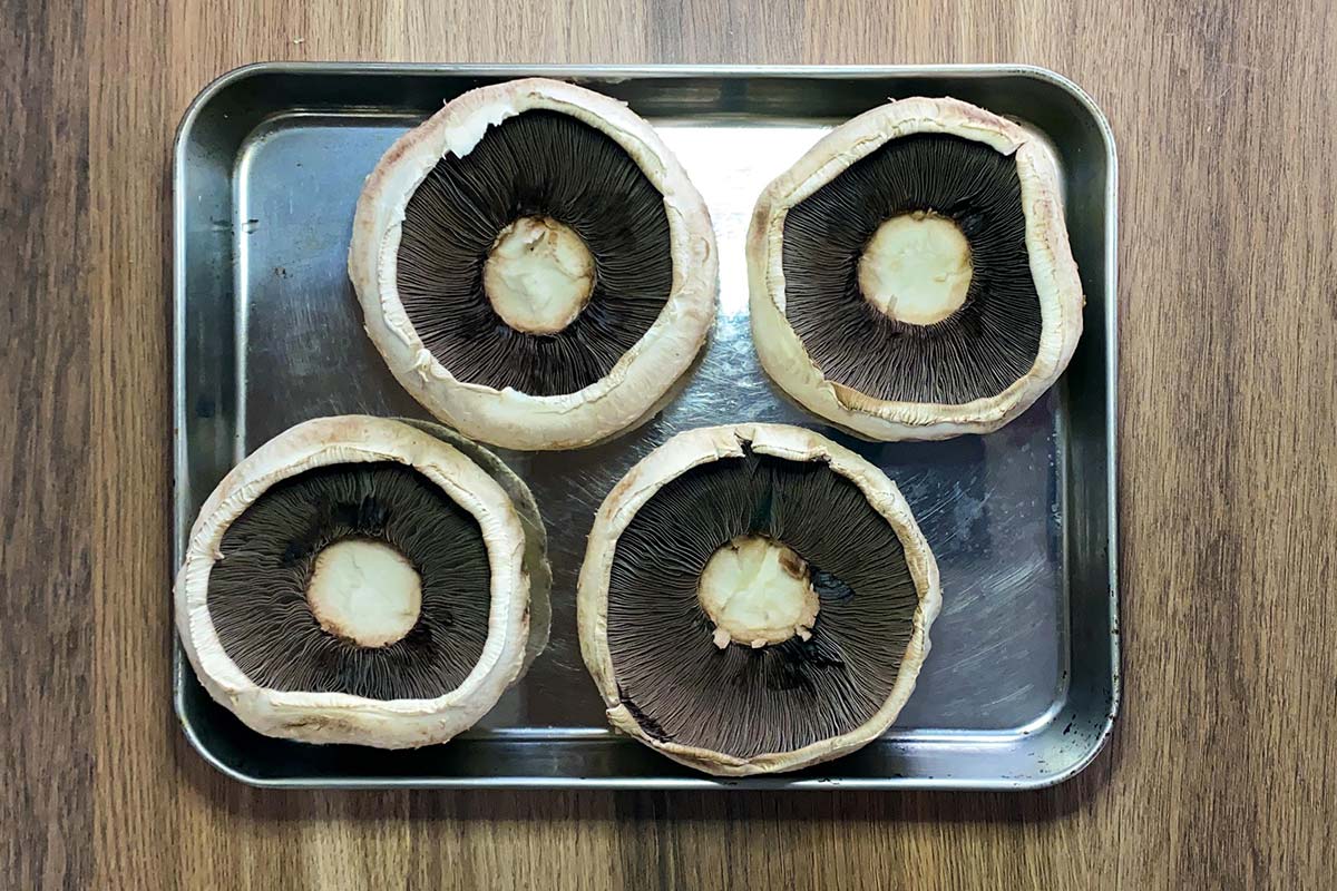 Four upturned portobello mushrooms on a baking tray.