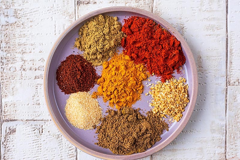 A plate with seven different small piles of spices.