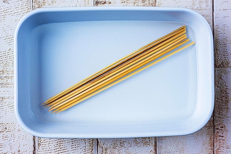 A rectangular dish with eight wooden skewers soaking in water.