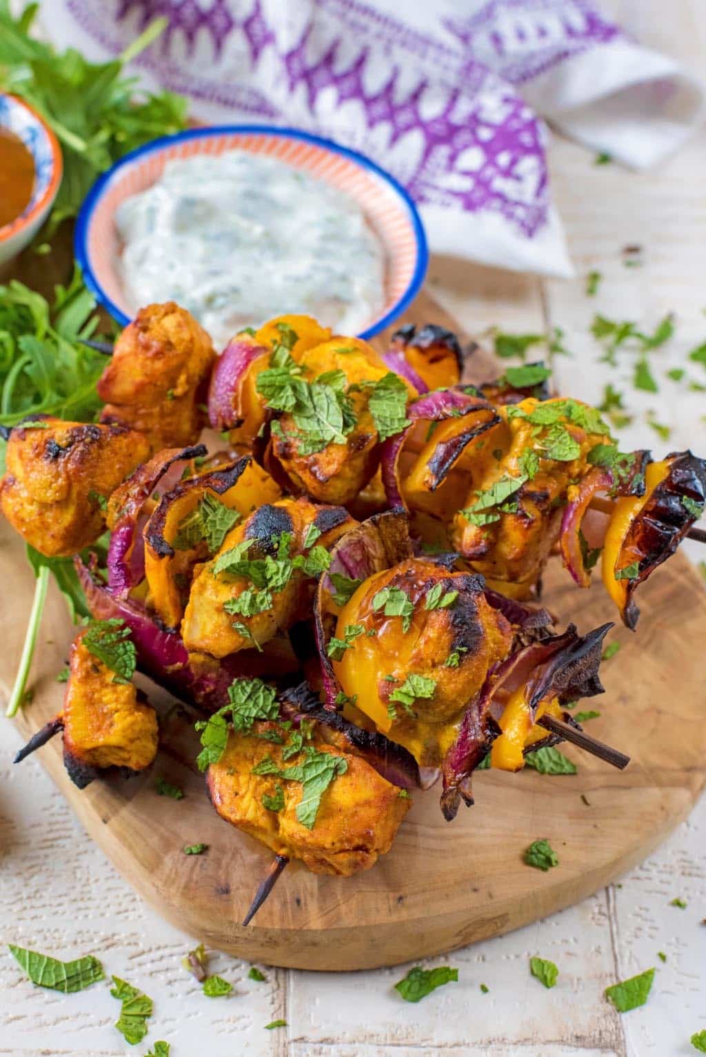 Four Chicken Tikka Kebabs on a wooden board in front of a white and purple towel.