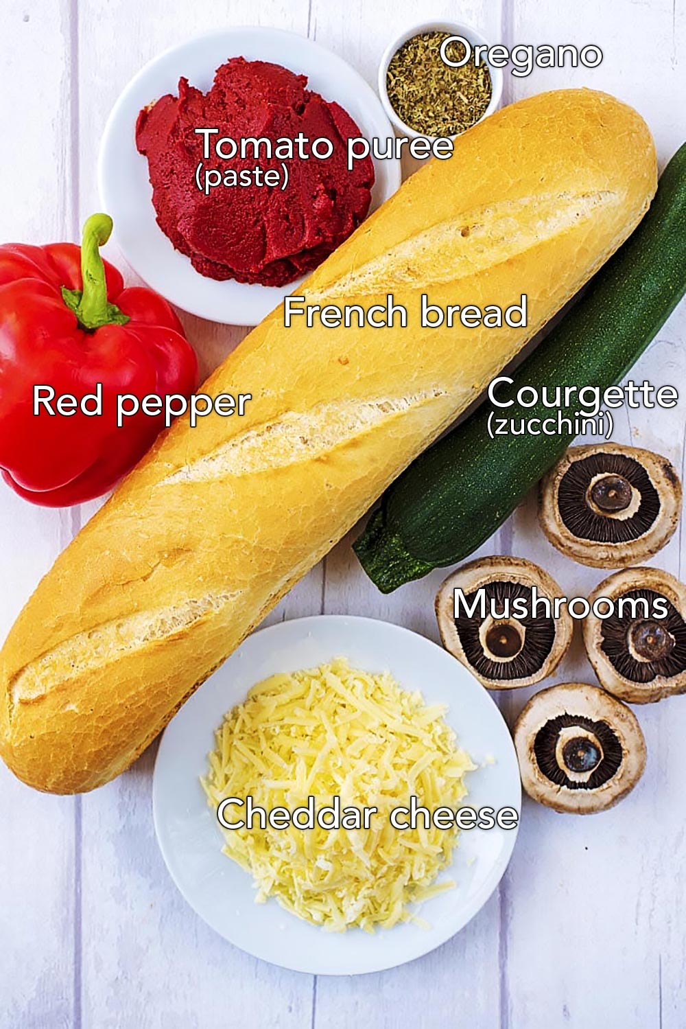 A french baguette, red pepper, mushrooms, courgette, cheese and tomato puree on a wooden surface.