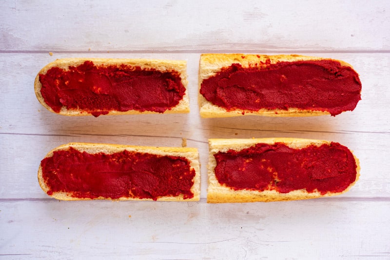 Four pieces of sliced French Bread spread with tomato paste.