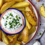 A plate of Garlic Potato Wedges surrounding a small dish of creamy dip