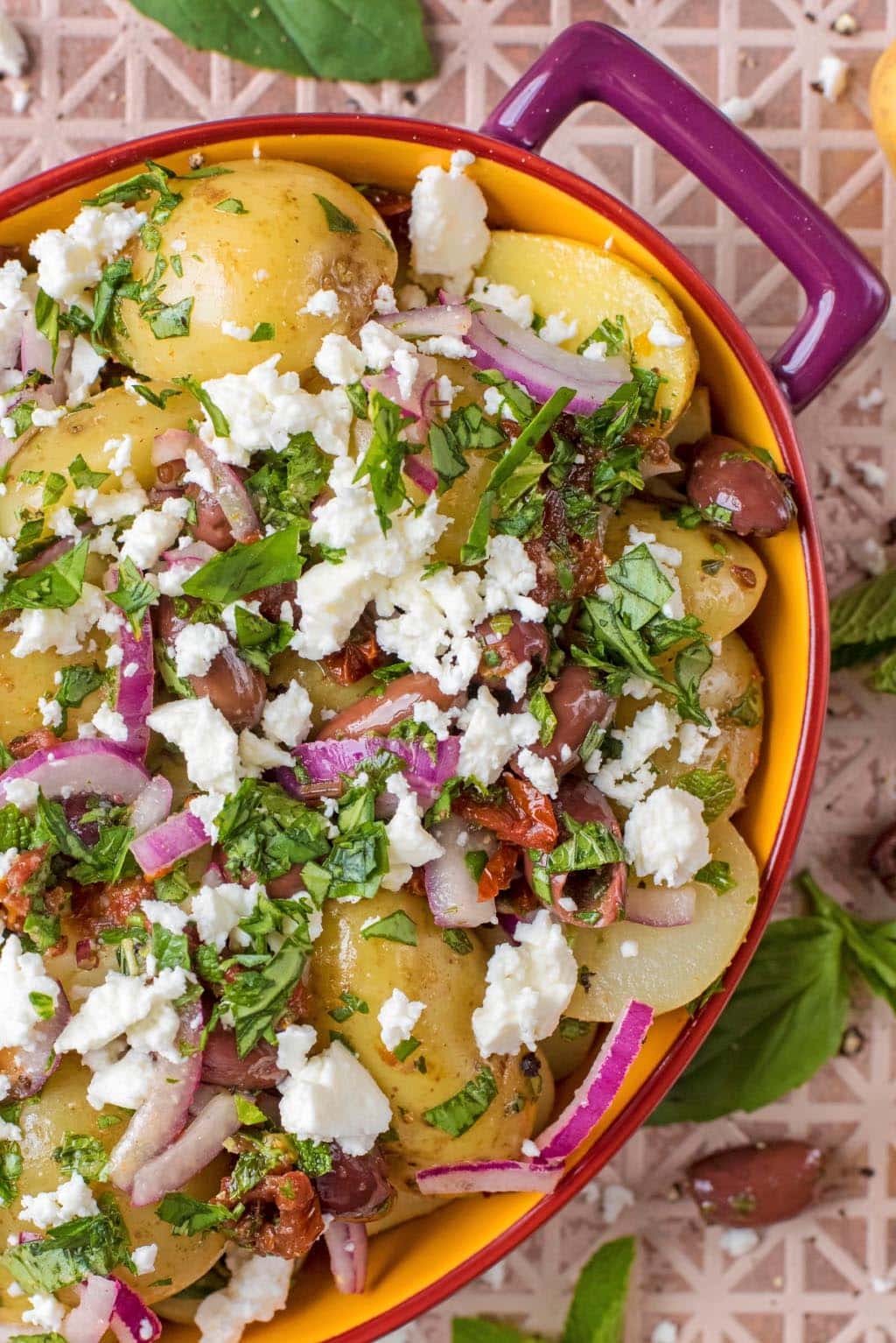 Mediterranean Potato Salad in an oval dish surrounded by basil leaves.