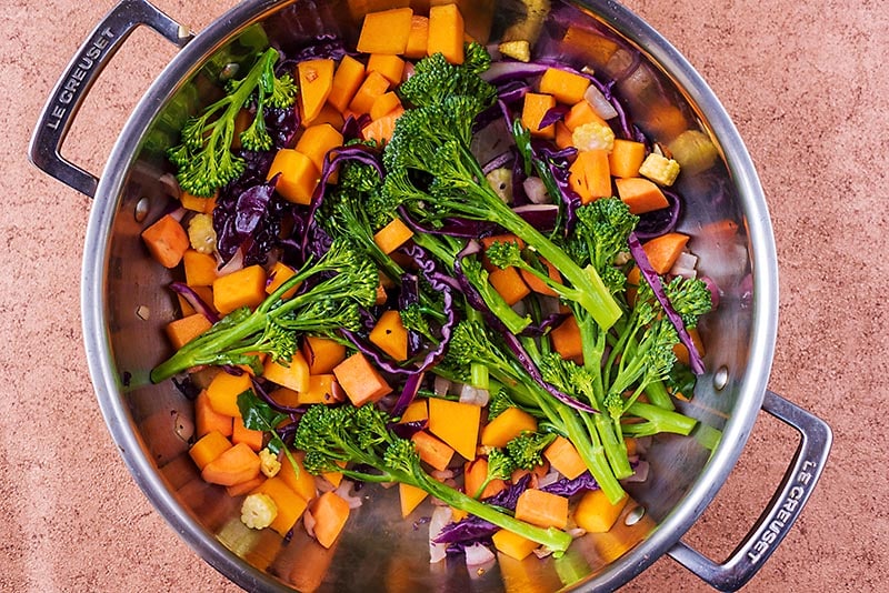 A large pan with cubed butternut squash, sweet potato, shallots and broccoli.