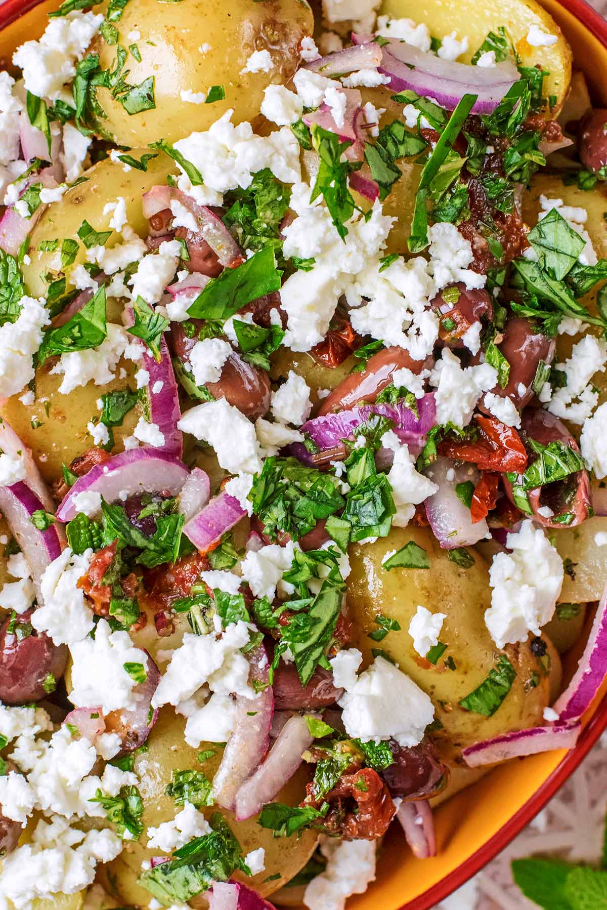 Chopped red onion, herbs, tomatoes and olives on top of cooked potatoes.