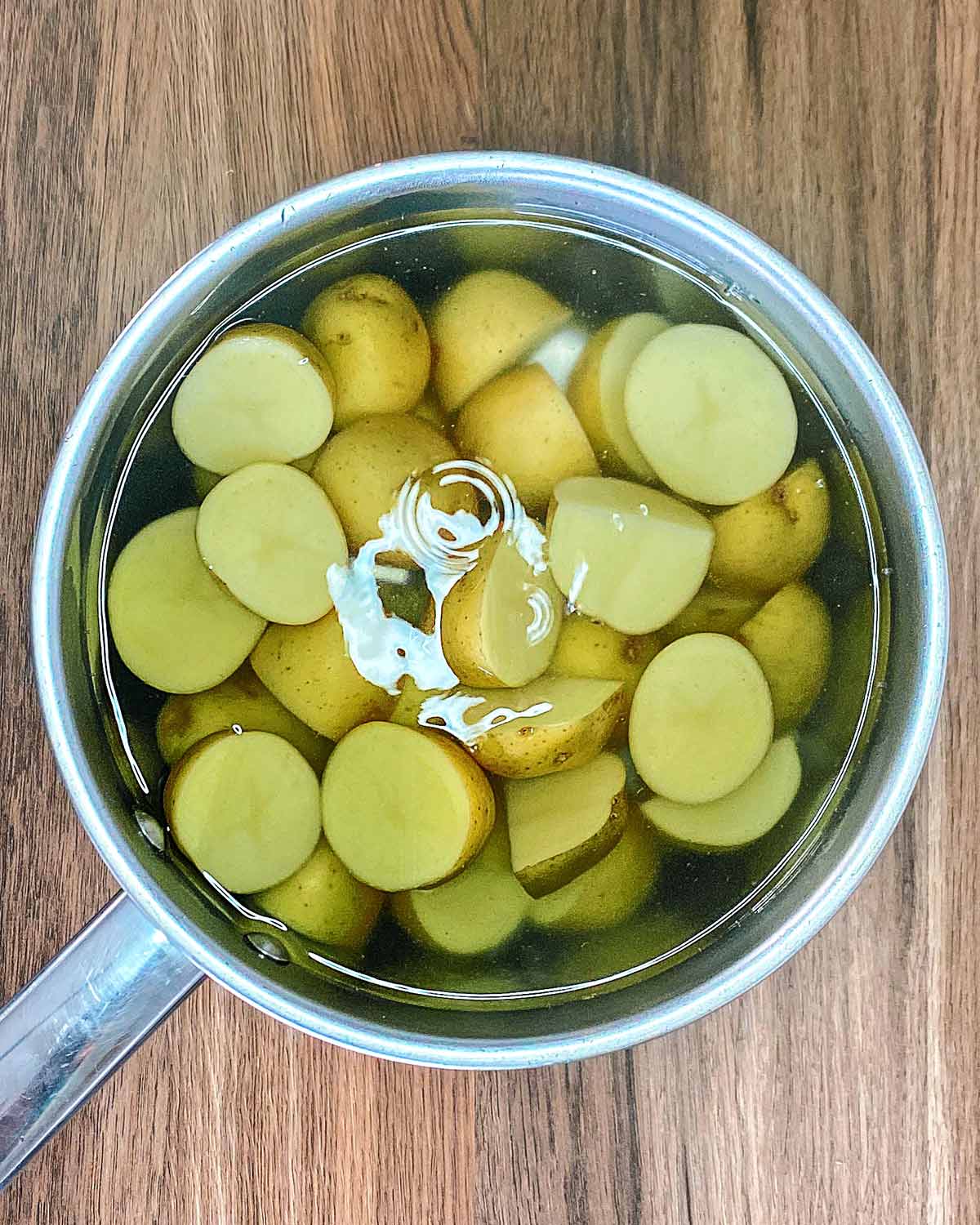 Halved new potatoes in a pan of salted water.