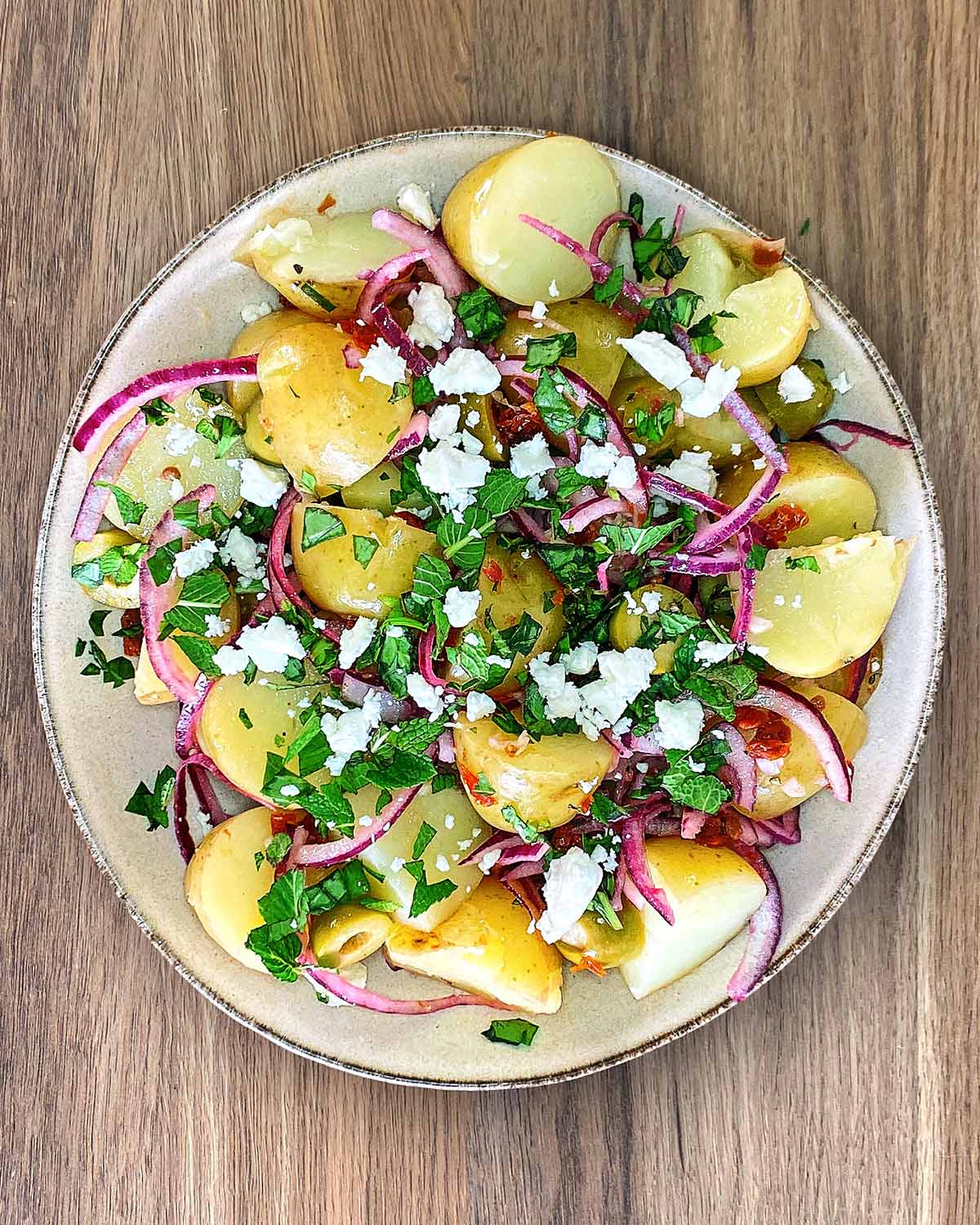 A plate with the potato salad topped with chopped herbs and crumbled feta cheese.