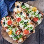 Four French Bread Pizzas on a round wooden serving board.