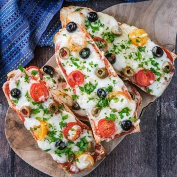 Four French Bread Pizzas on a round wooden serving board.