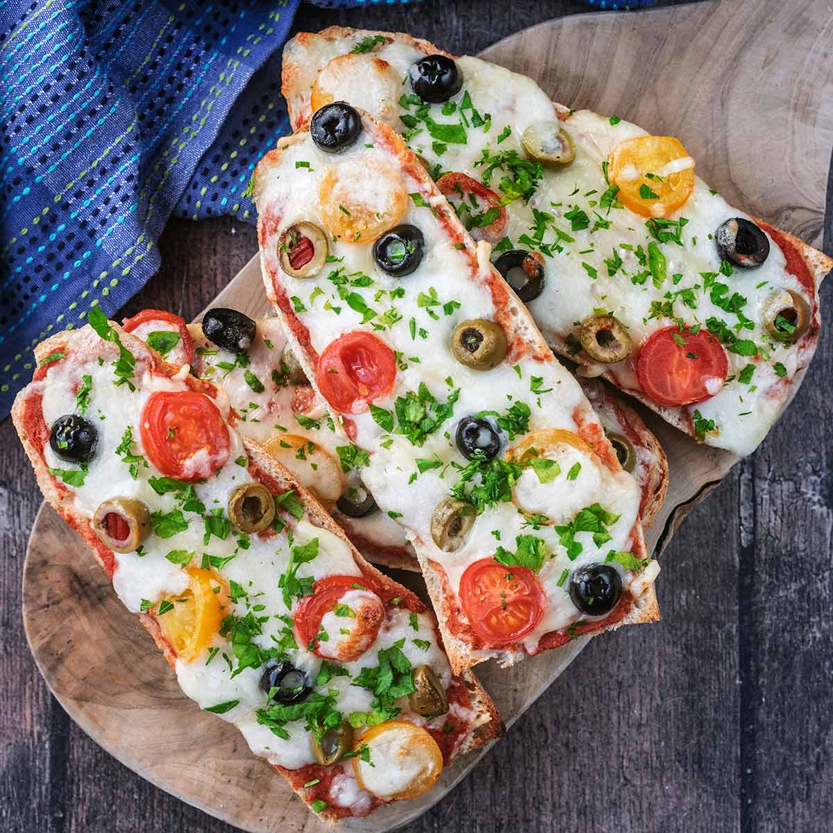 Four French Bread Pizzas on a round wooden serving board.