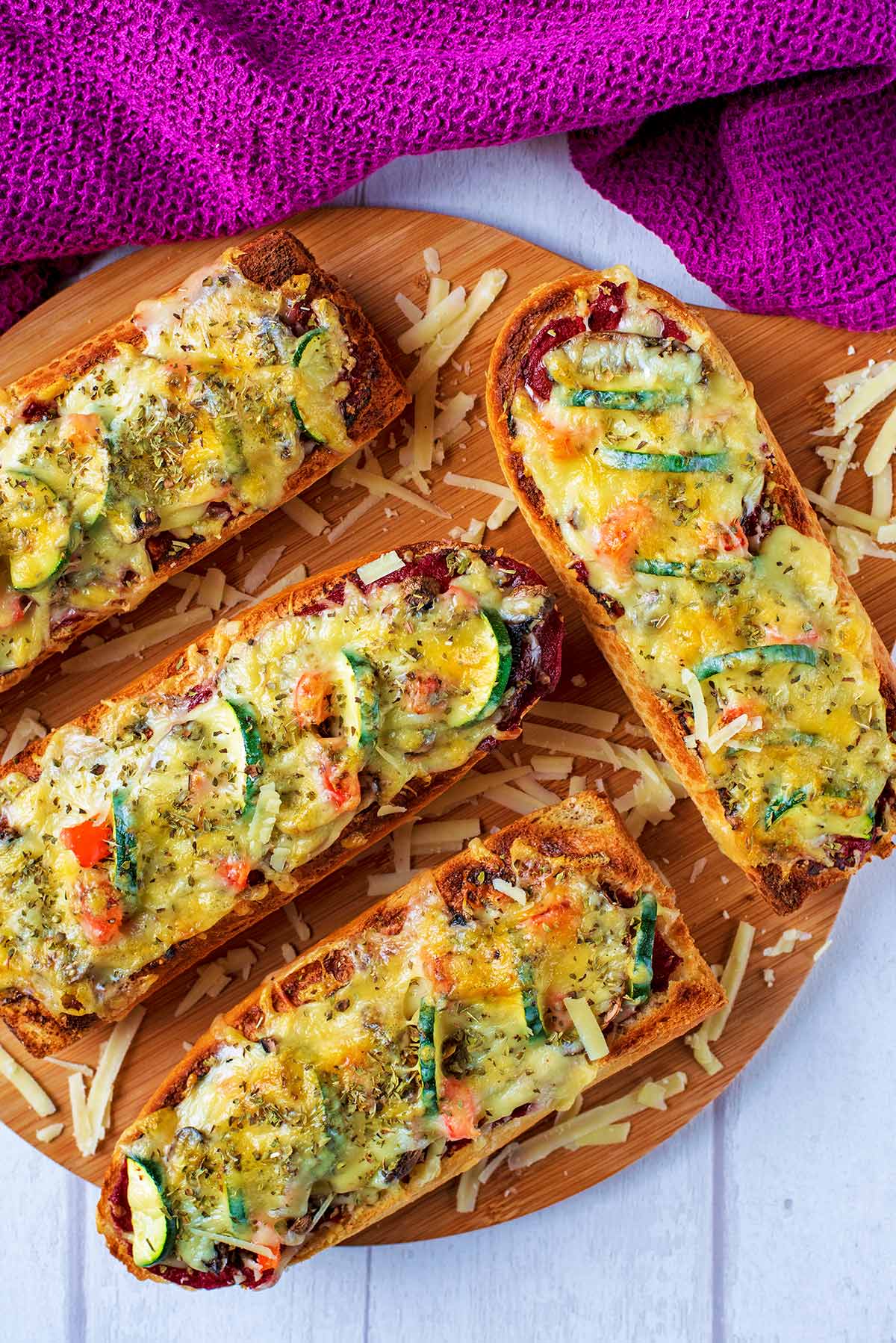 French bread pizzas on a round wooden serving board.