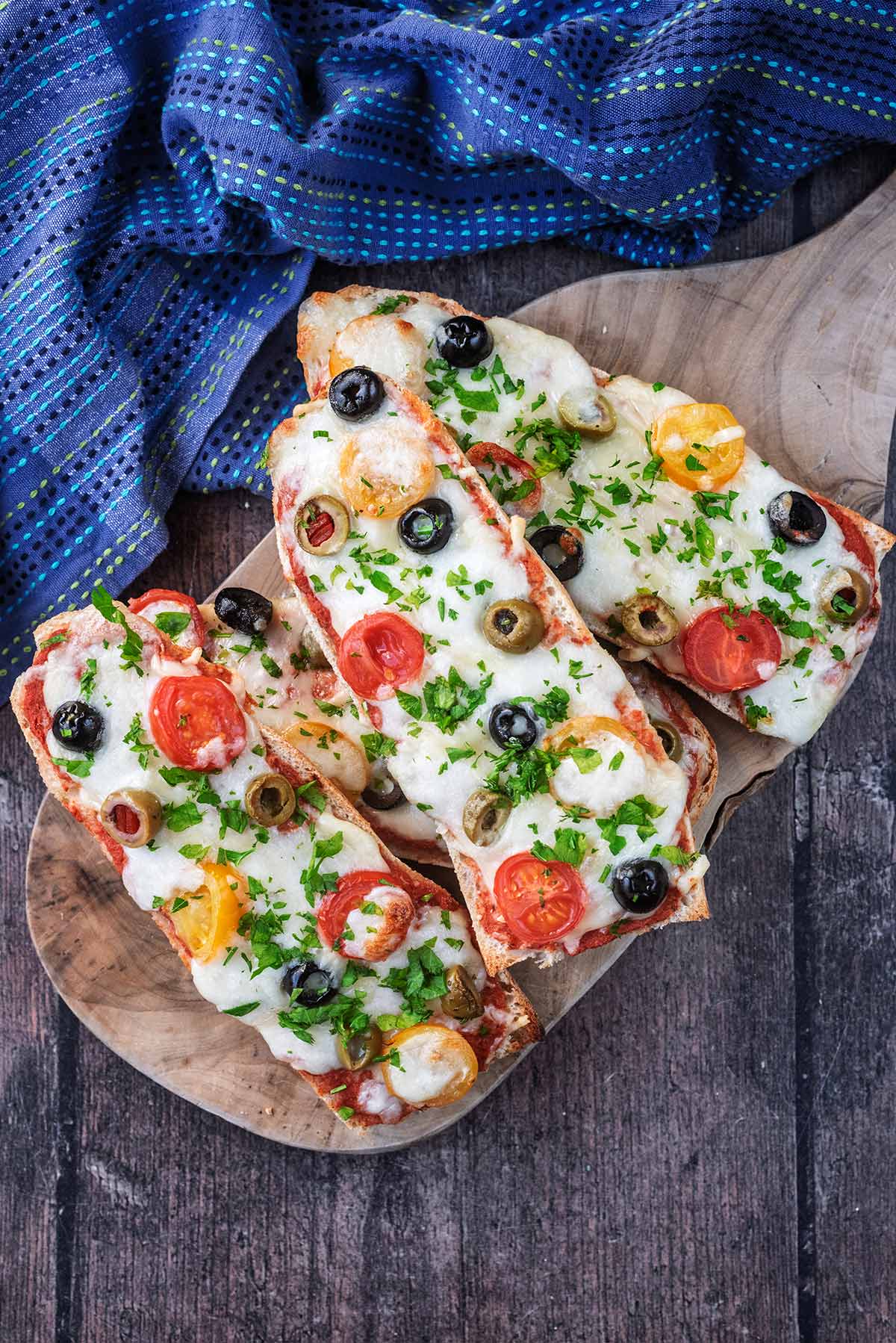 Four French bread pizzas stacked on a wooden serving board.
