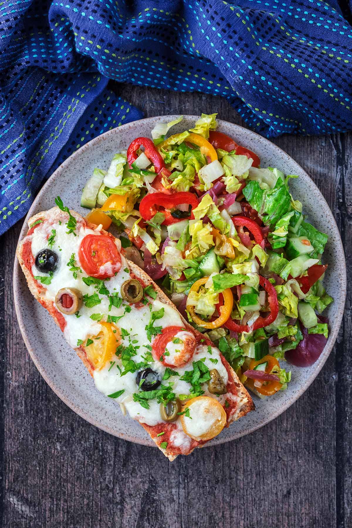 A plate with a slice of French bread pizza and a chopped salad.