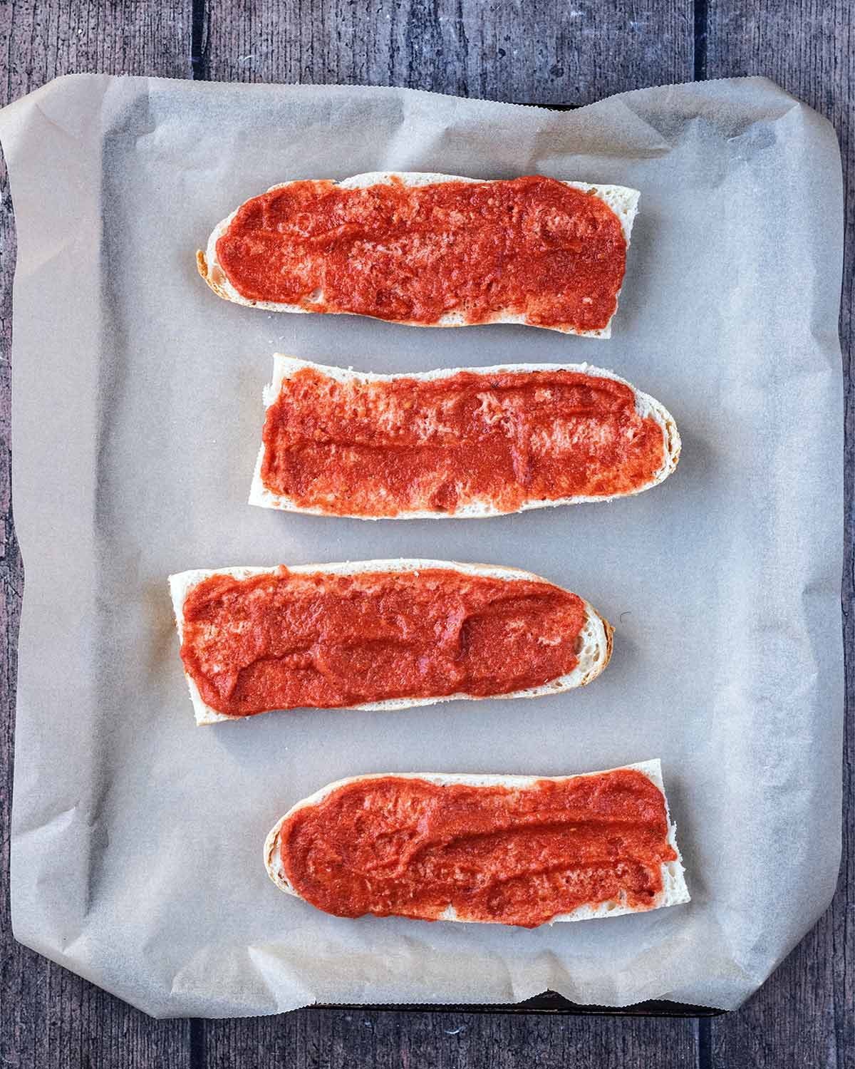 Four pieces of sliced French Bread spread with pizza sauce.