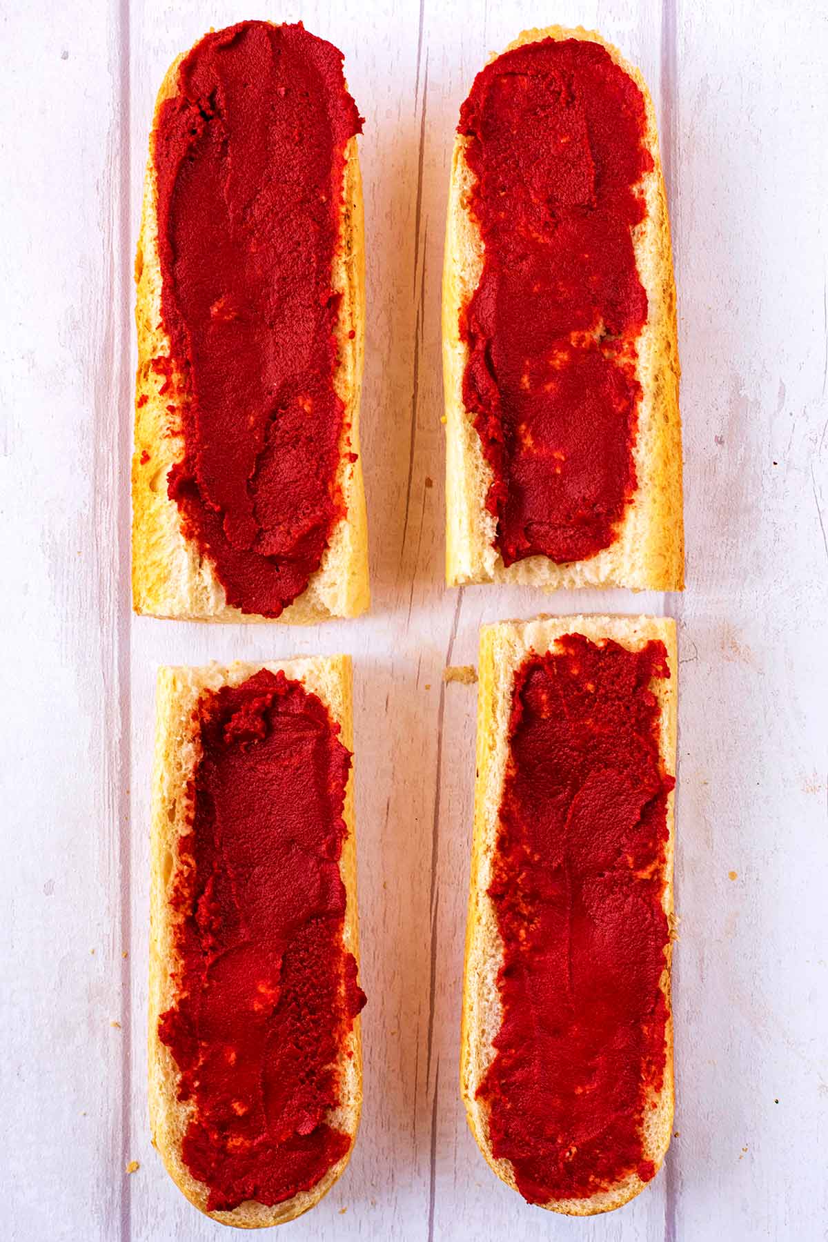 Four pieces of sliced French Bread spread with tomato paste.