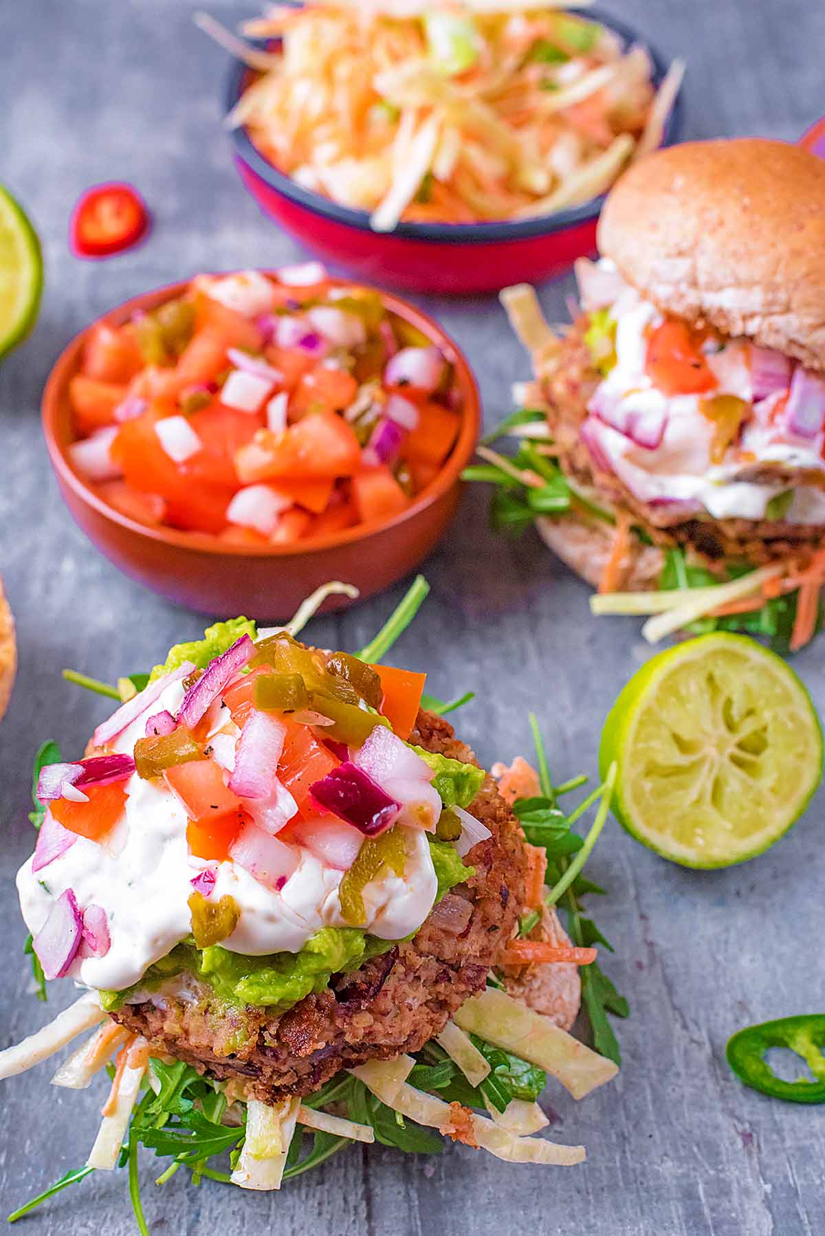 A bean burger on a bun bottom topped with guacamole, yogurt and salsa.