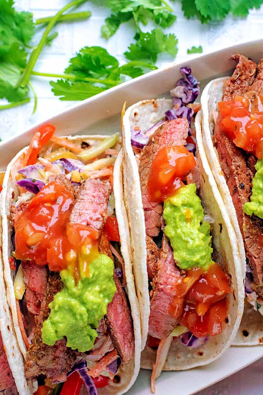 Steak tacos topped with salsa and guacamole.