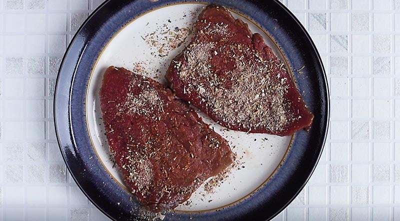 A plate with two pieces of steak, covered in seasoning.