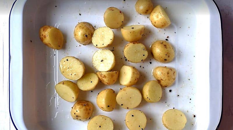 A roasting tin with halved baby potatoes and seasoning.