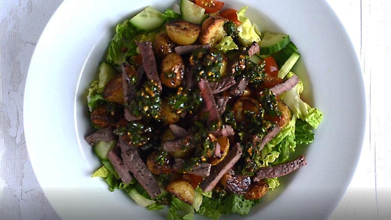 A bowl of steak salad with chermoula drizzled over it.