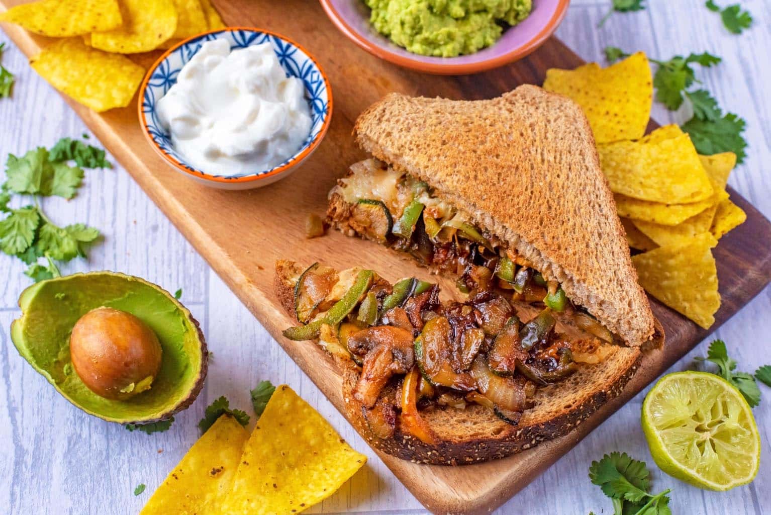 Fajita sandwich on a serving board with tortilla chips and guacamole.