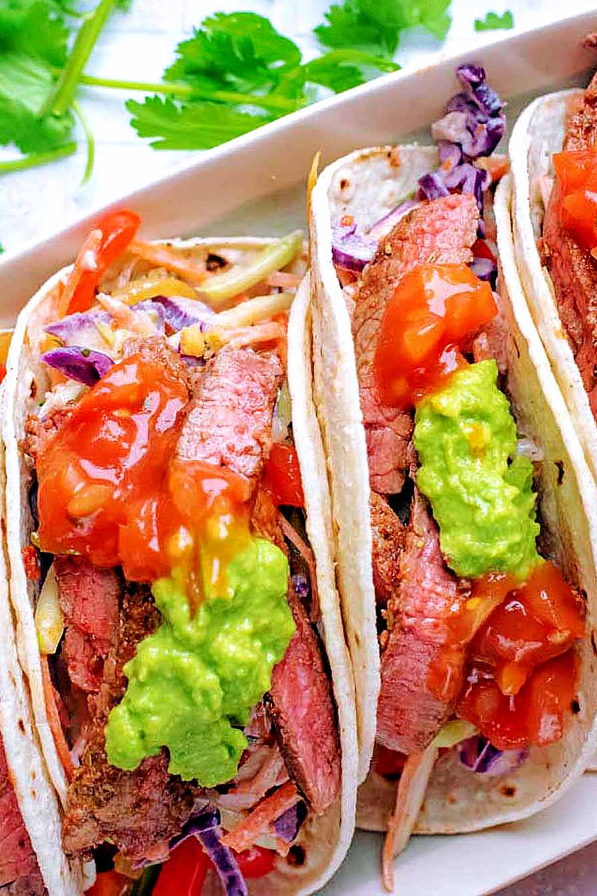 Steak tacos topped with salsa and guacamole.