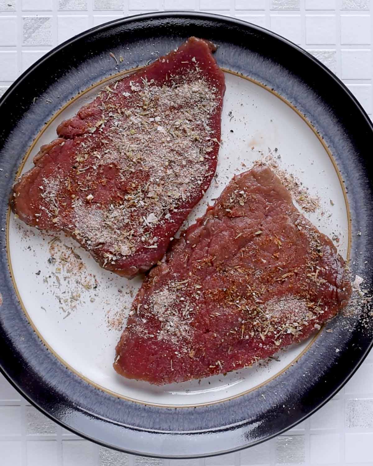 A plate with two pieces of steak, covered in seasoning.
