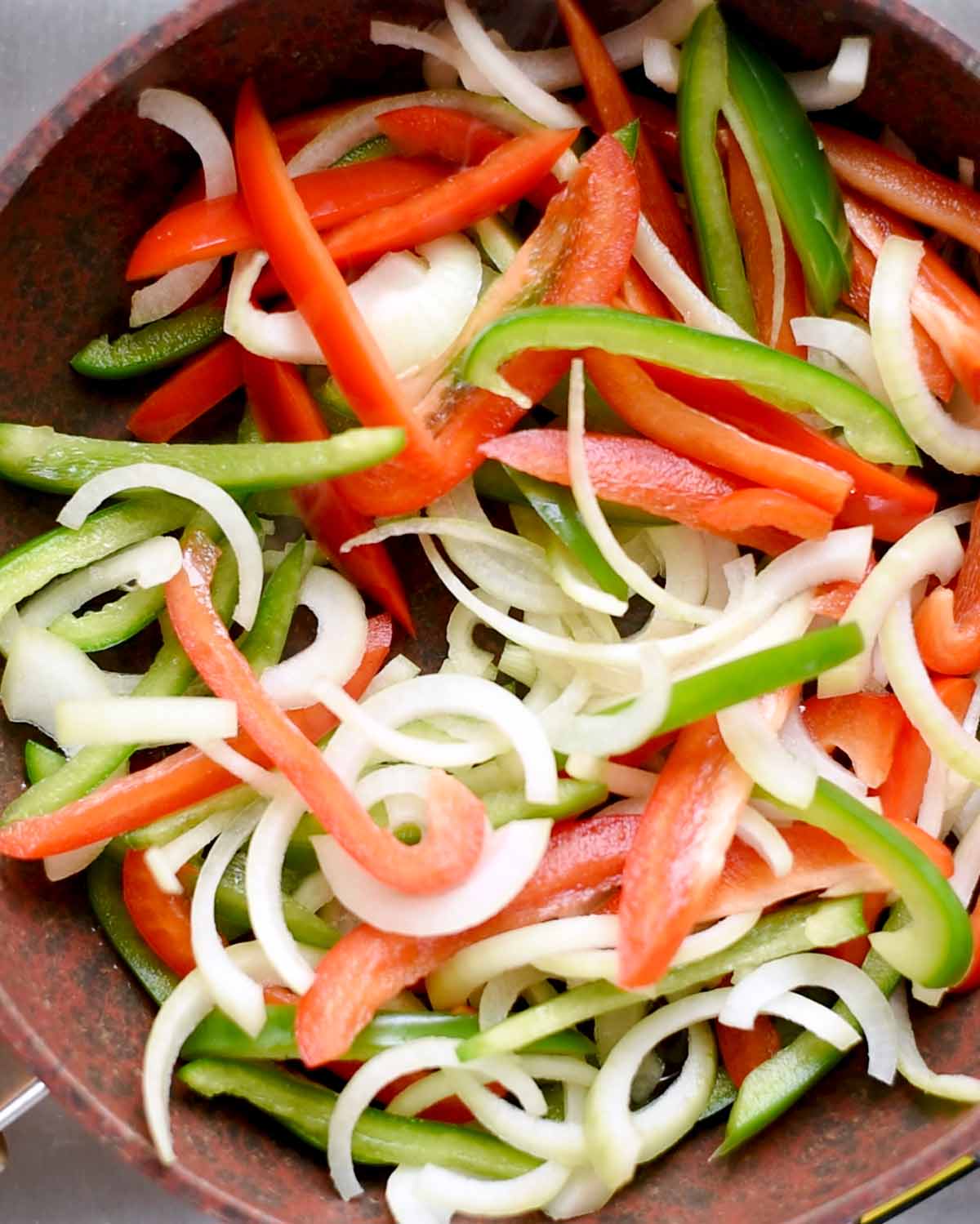 A large pan with thinly sliced onions and peppers.