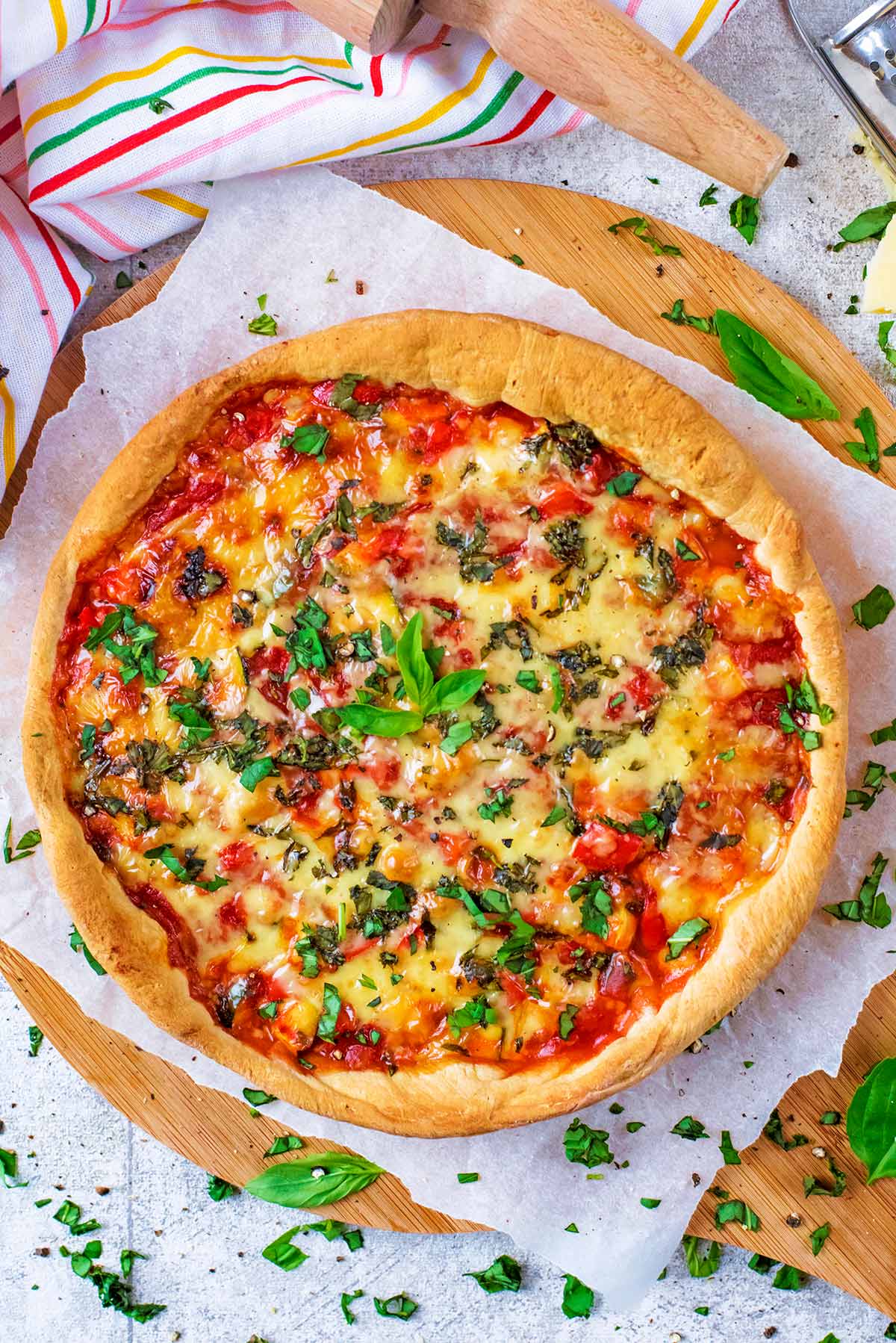 A whole deep dish pizza topped with herbs, sat on some parchment paper.