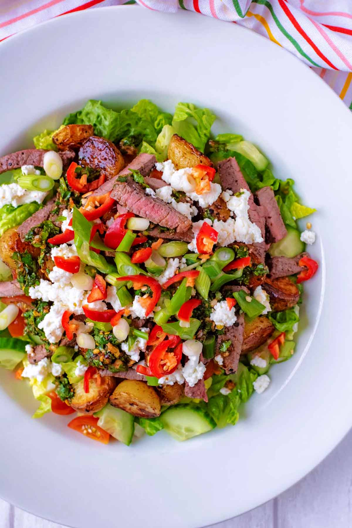A bowl of steak and potato salad next to a colourful striped towel.