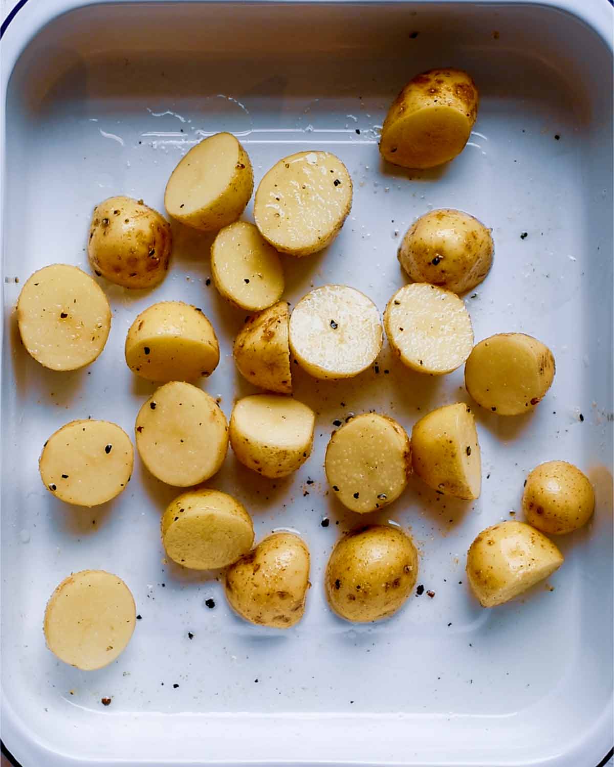 A roasting tin with halved baby potatoes and seasoning.
