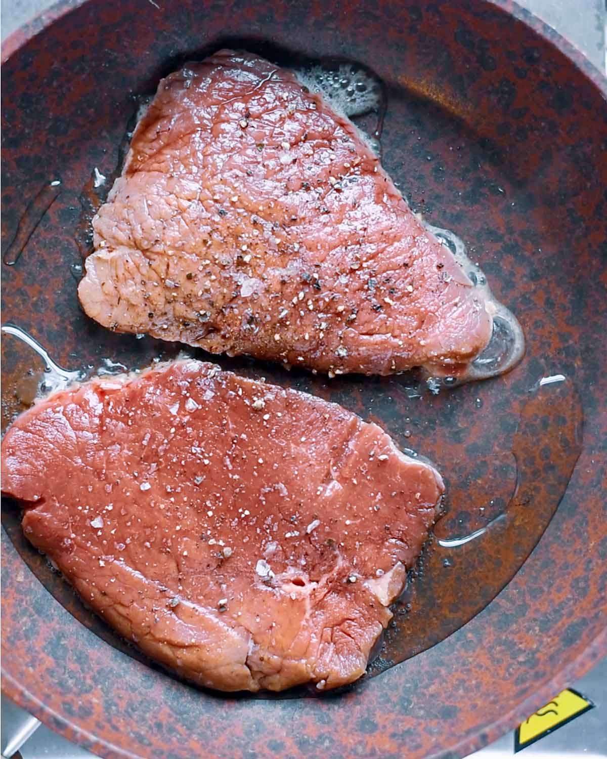 Two pieces of steak frying in a pan.