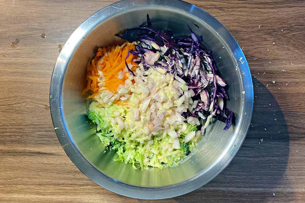 Shredded cabbage, grated carrot, chopped onions and brocoli in a bowl with dressing poured over.