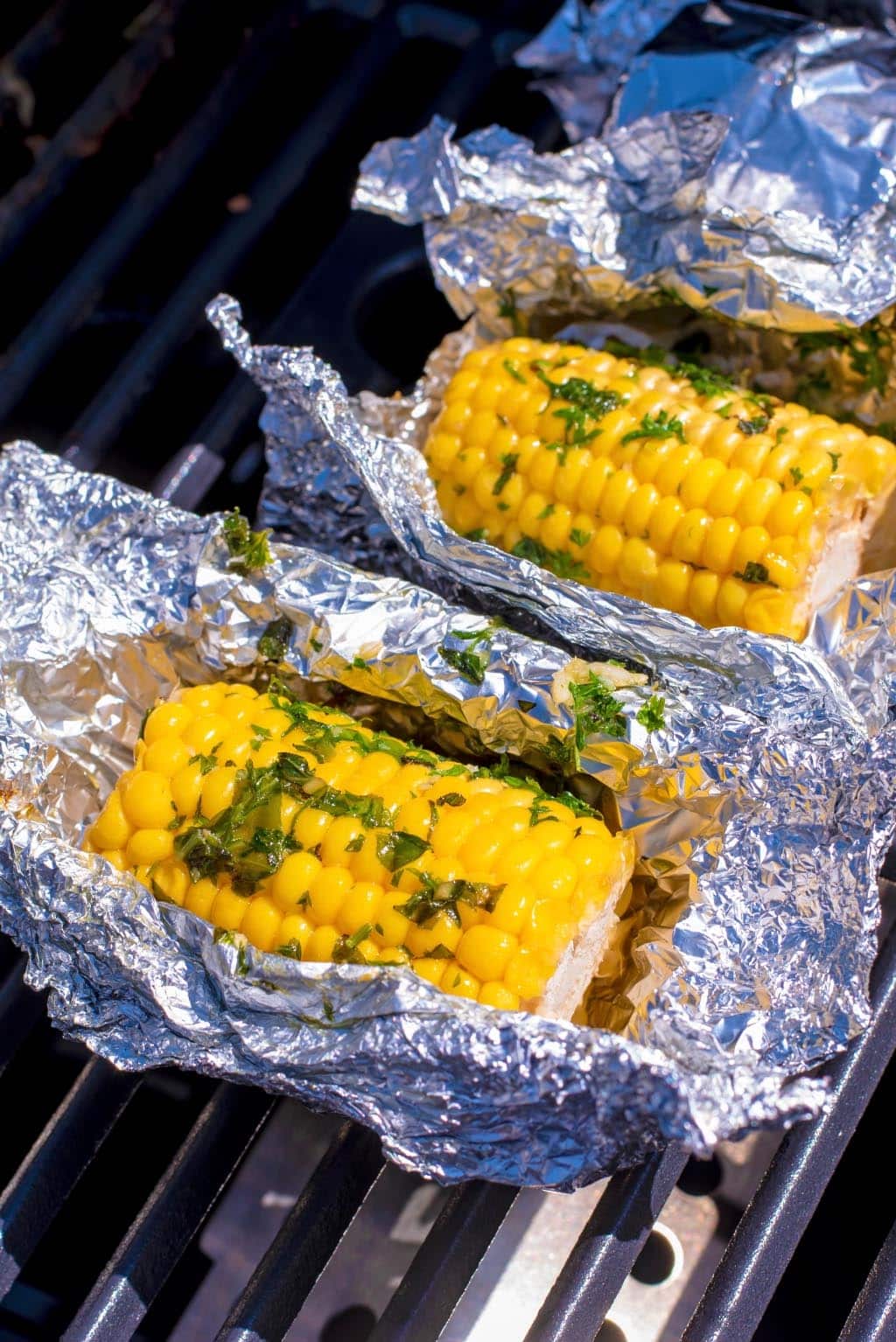 Corn wrapped in open foil on a barbecue grill.