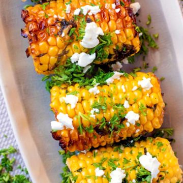 Grilled corn on the cob topped with crumbled cheese and chopped herbs.