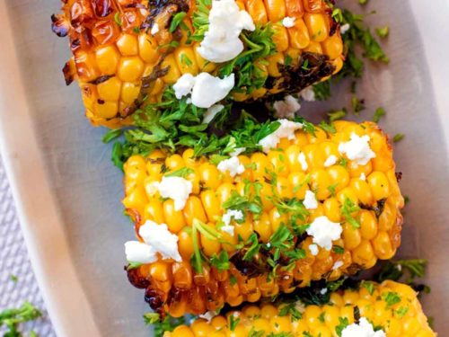 Grilled corn on the cob topped with crumbled cheese and chopped herbs.