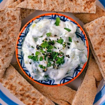 Tzatziki surrounded by sliced pita on a blue and white plate.