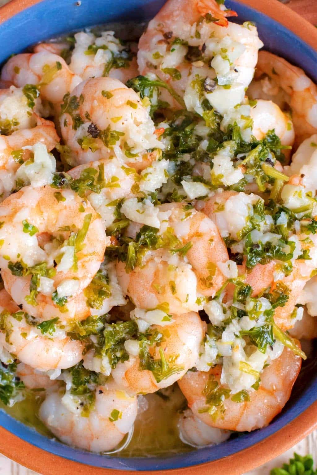 Cooked shrimp in a bowl covered in garlic and chopped herbs.