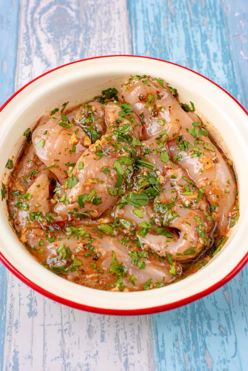 Bowl of Chicken strips marinating in herbs, spices and oil.