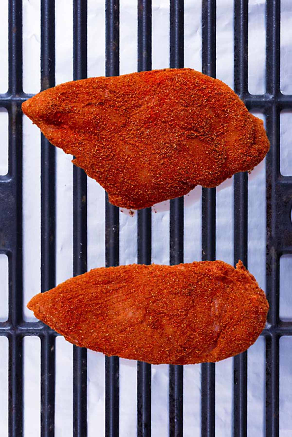 A barbecue grill with two seasoned chicken breasts on it.