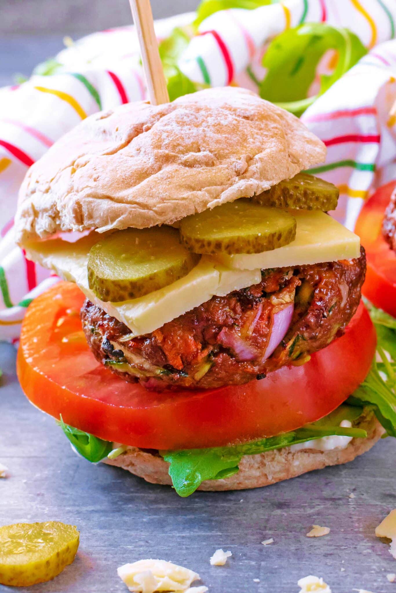 A burger made up of bun, lettuce, tomato, beef patty, cheese and pickles.