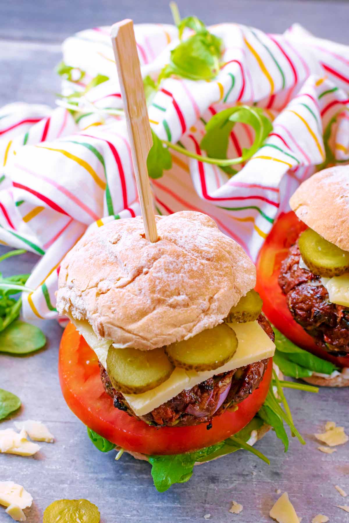 A beef burger in a bun with salad, cheese and pickles. A small wooden skewer is pushed through the whole burger.